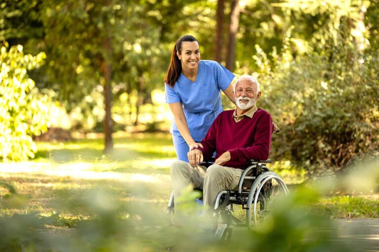 Older resident speaking with a visitor in a bright assisted living lounge beside a daily activity calendar.